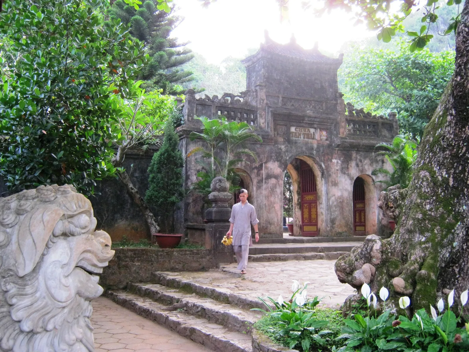 Một người đàn ông đi bộ qua sân đá của chùa Tam Thái cổ kính giữa cây xanh gần Đà Nẵng.