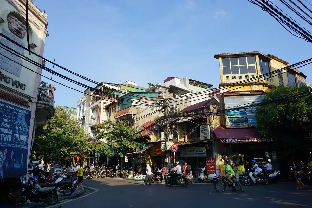 Một góc phố đông đúc ở Phố Cổ Hà Nội với những ngôi nhà cũ, dây điện chằng chịt và xe máy qua lại.